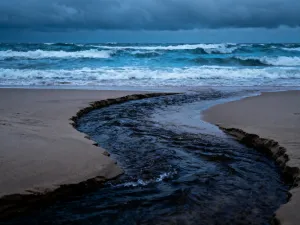 Kobieta wypoczywająca na leżaku na słonecznej plaży Costa Brava w październiku, z widokiem na turkusowe morze.